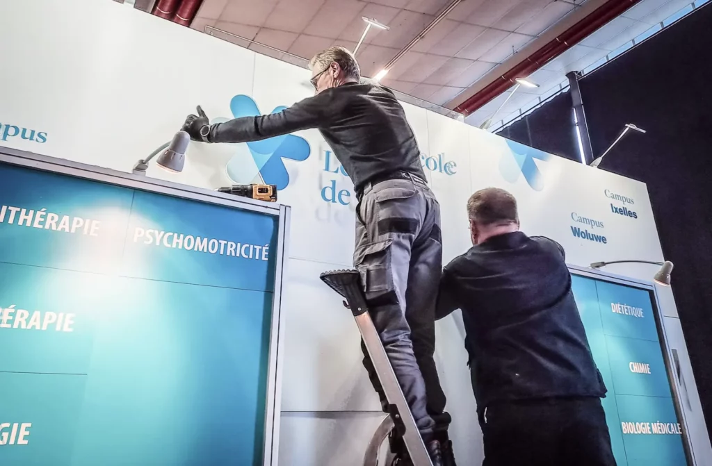 Montage d’un stand d’exposition par deux ouvriers dans un espace événementiel